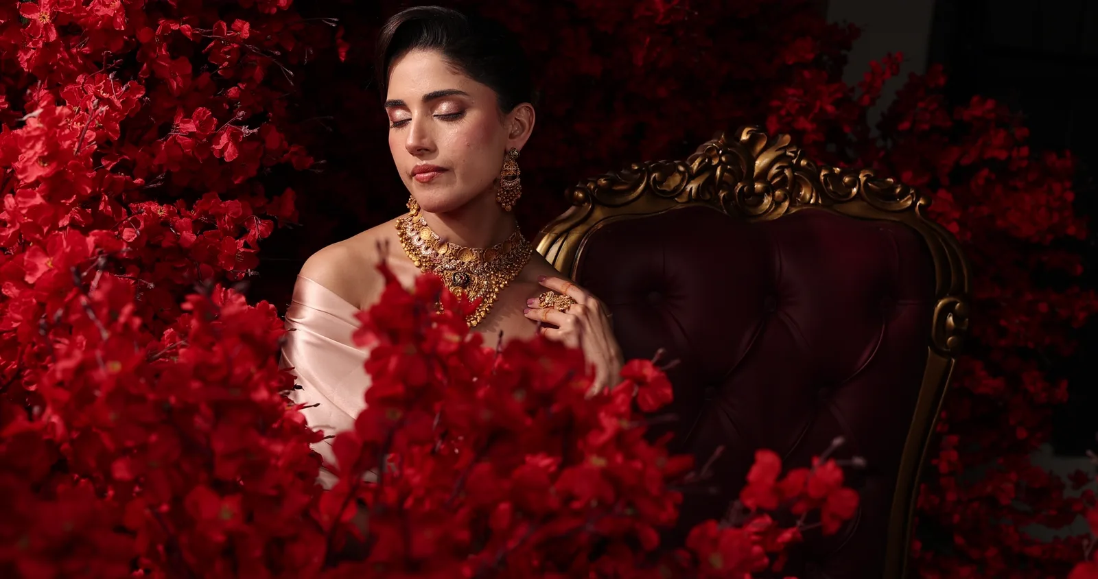 A woman in a champagne satin drape wearing the temple collar, seated among red roses